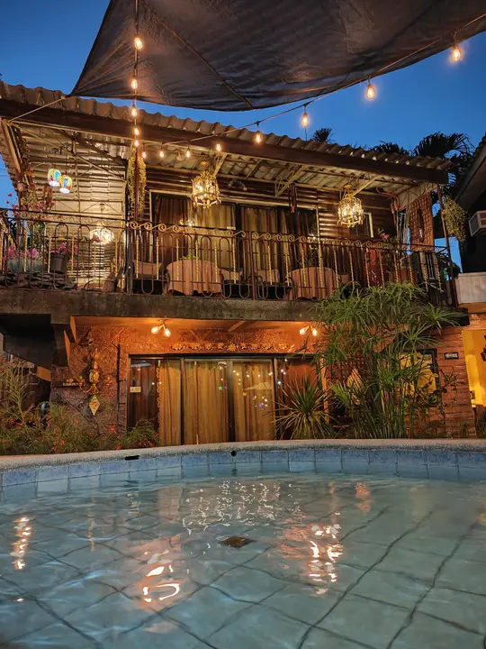 The hot spring pool at Cayet's Cabin at night, under string lights, with the wooden two-storey cabin behind