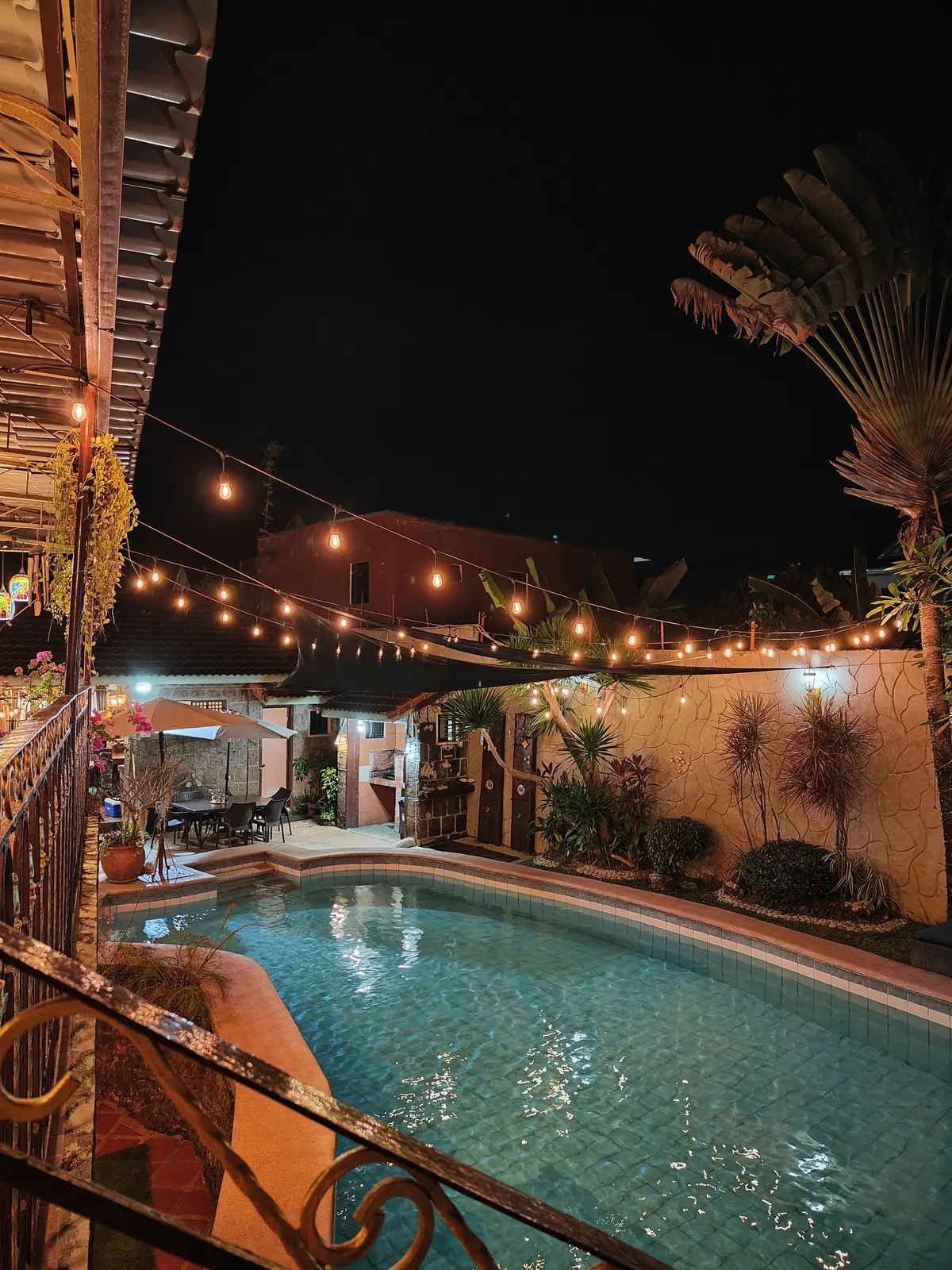 The adult hot spring pool at night with festoon lights and the cabin behind
